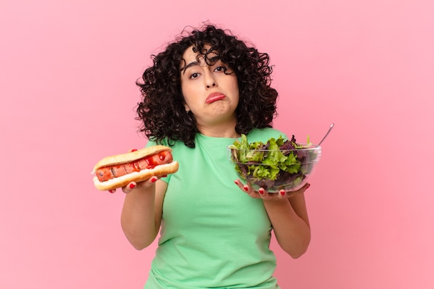 Jolie femme arabe tenant une salade et un hot-dog. concept de régime