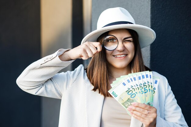 Jolie femme avec de l'argent dans ses mains et une loupe Femme examine les billets dans ses mains