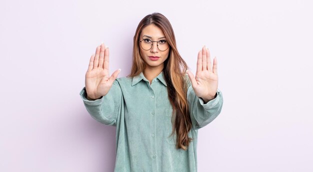 Jolie femme asiatique à l'air sérieuse, malheureuse, en colère et mécontente interdisant l'entrée ou disant stop avec les deux paumes ouvertes