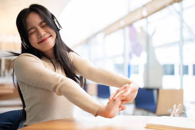 Une jolie femme asiatique apprécie la musique et étire ses bras tout en se détendant à une table