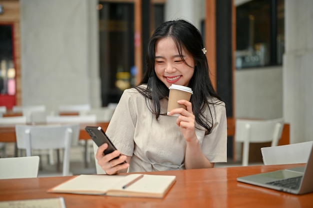 Une jolie femme asiatique envoie des SMS à ses amis tout en travaillant à distance dans un café