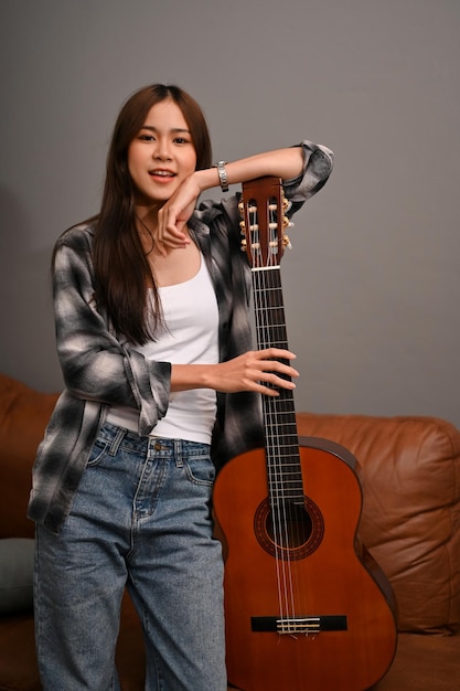 Jolie femme asiatique hipster dans son salon moderne et chic vintage avec une guitare acoustique