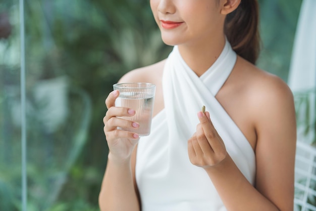 Une jolie femme asiatique millénaire tient une pilule et un verre d'eau