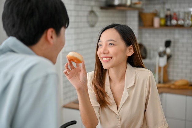 Jolie femme asiatique nourrissant un beignet à son petit ami s'amusant ensemble dans la cuisine