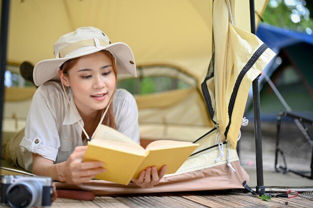 Jolie femme asiatique se détend en lisant un livre et allongée dans sa tente au camping