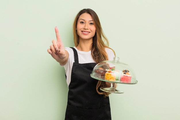 Jolie femme asiatique souriant fièrement et en toute confiance faisant le concept de gâteaux faits maison numéro un