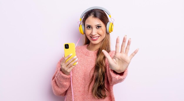 Jolie femme asiatique souriante et semblant amicale, montrant le numéro cinq. casque et concept de téléphone