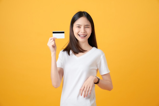 Jolie femme asiatique souriante tenant le paiement par carte de crédit sur le mur jaune