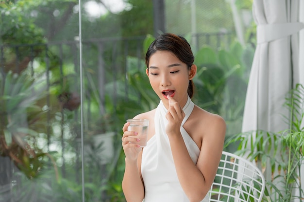 Jolie Femme Asiatique Tenant Un Verre D'eau Minérale En Prenant La Pilule En Détournant Les Yeux