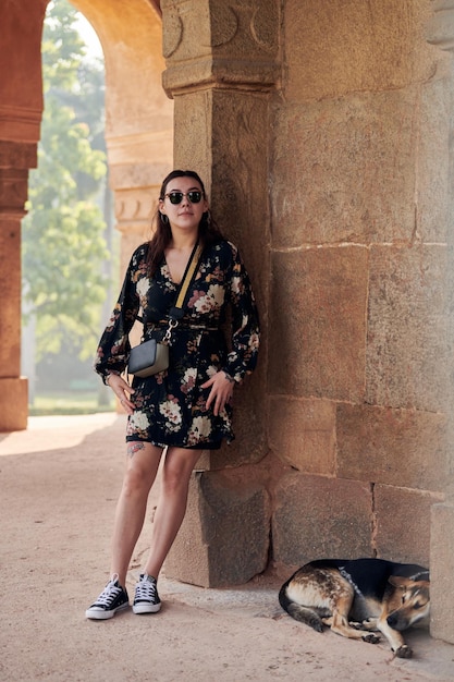 Jolie femme d'Asie de l'Est en robe noire de lunettes de soleil se tient près d'un chien couché dans une ancienne tombe indienne