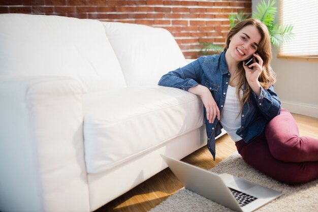 Jolie femme assise sur le sol, appelant au téléphone dans le salon