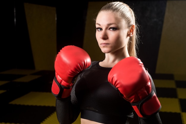 Jolie femme athlétique en gants de boxe rouges posant dans la salle de gym