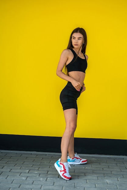 Jolie femme athlétique en vêtements de sport noirs près du mur jaune. mode de vie sain