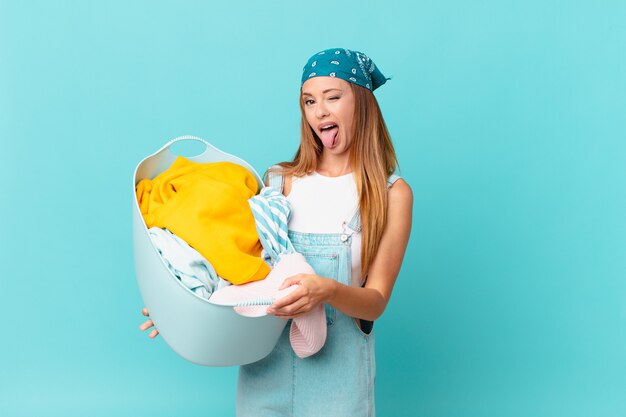 Jolie femme avec une attitude joyeuse et rebelle, plaisantant et tirant la langue tenant un panier de lavage