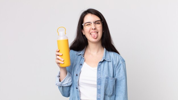 Jolie femme avec une attitude joyeuse et rebelle, plaisantant et tirant la langue et tenant un thermos de café