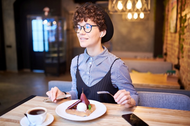 Jolie femme au chapeau et chic décontracté assis par table au café, se détendre et savourer un dessert savoureux