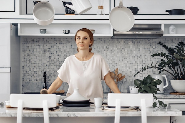 Une jolie femme au foyer blonde est sur le point de préparer de la nourriture pour sa famille depuis la cuisine à lumière blanche. Notion de soins