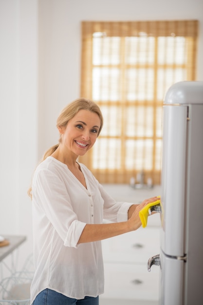 Jolie femme au foyer blonde nettoyant le frigo