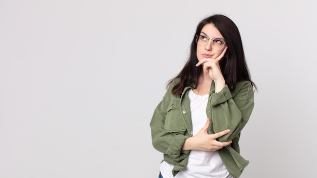 Jolie femme au regard concentré, se demandant avec une expression douteuse, levant les yeux et sur le côté