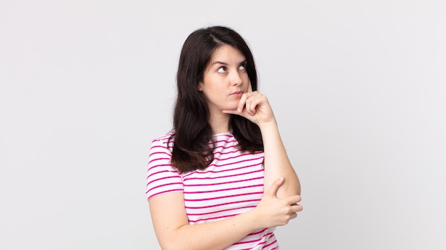 Jolie femme au regard concentré, se demandant avec une expression douteuse, levant les yeux et sur le côté