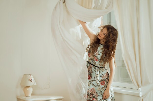 Jolie femme aux cheveux bouclés enlevant le rideau