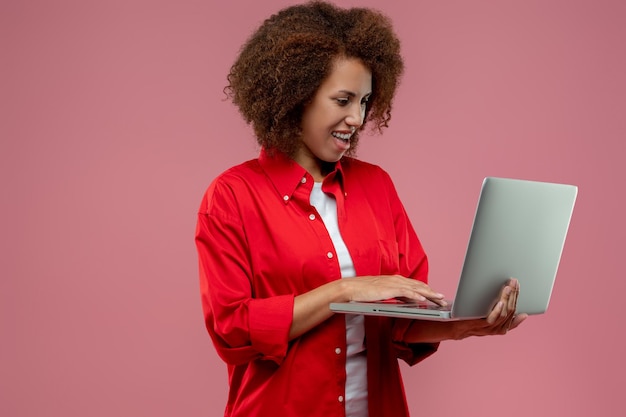 Jolie femme aux cheveux bouclés en veste rouge travaillant sur un ordinateur portable