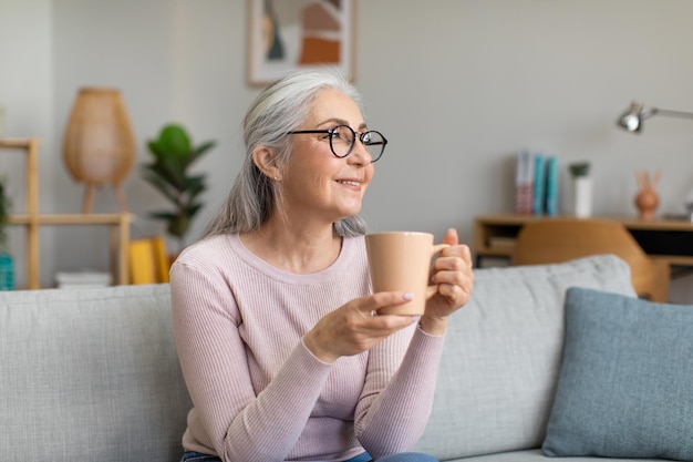 Jolie femme aux cheveux gris d'âge caucasien souriante dans des verres se reposant et appréciant un verre regarde l'espace de copie