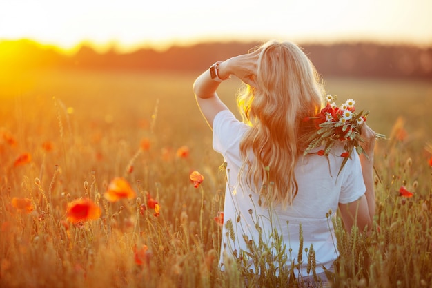 Jolie femme aux cheveux longs sur champ de pavot au coucher du soleil.