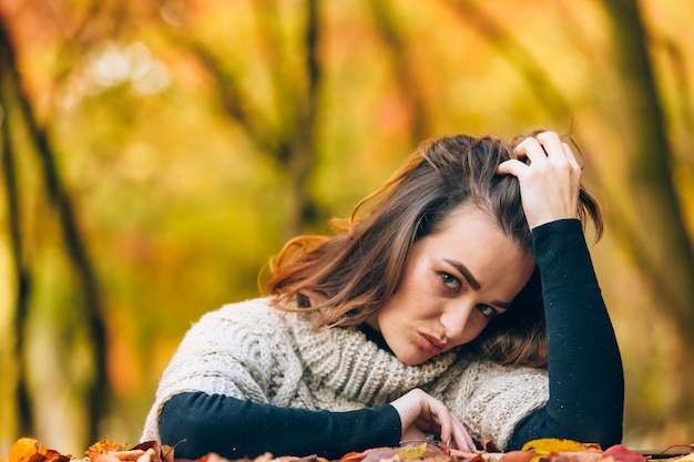 Jolie femme aux cheveux luxueux repose sa tête sur sa main sur le fond d'un parc en automne. Fermer