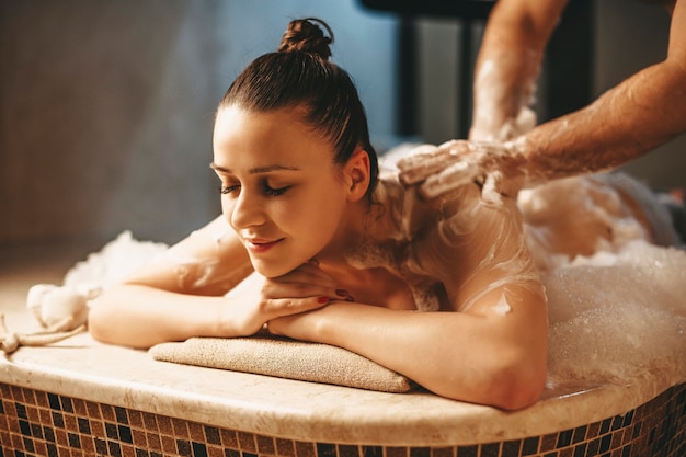 Jolie femme aux cheveux noirs ayant un massage relaxant avec de la mousse dans un hammam turc spa bien-être.