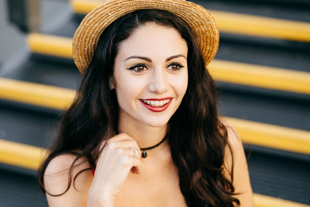 Jolie femme aux cheveux noirs, yeux, peau pure et lèvres rouges portant chapeau de paille