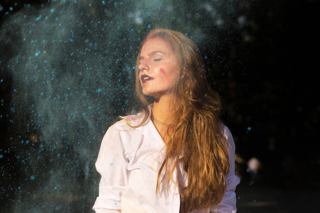 Jolie femme aux cheveux rouges en chemise blanche posant avec de la peinture sèche Holi qui explose