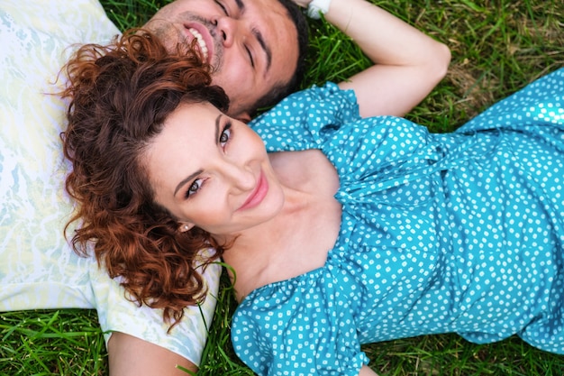 Jolie femme aux cheveux rouges en robe bleue et jeune homme allongé sur l'herbe