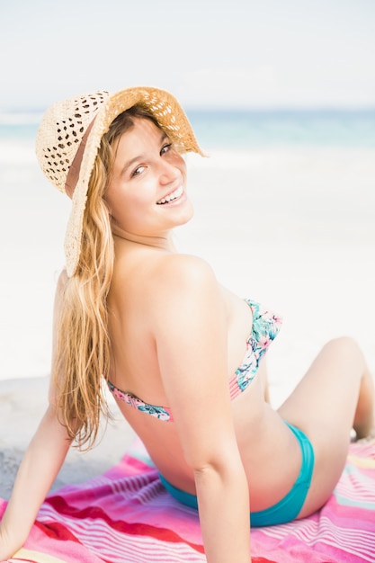 Jolie femme en bikini et chapeau de plage assis sur la plage