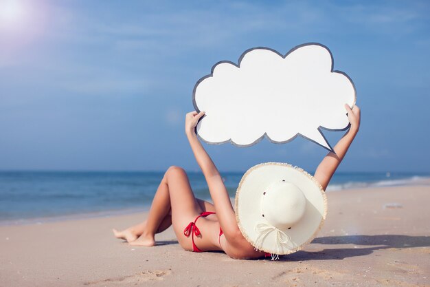 Jolie femme en bikini avec discours de bulle dans les mains sur la plage