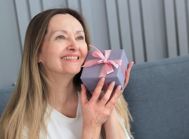 Une jolie femme blonde âgée tenant une boîte-cadeau se sent heureuse Événements de la vie