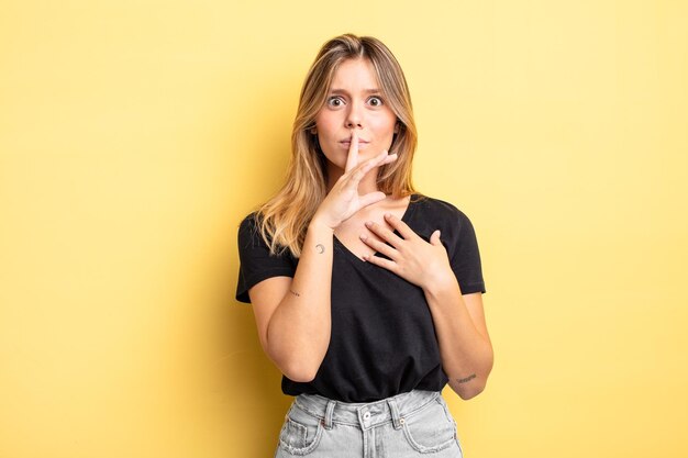 Jolie femme blonde à l'air sérieuse et croisée avec le doigt pressé sur les lèvres exigeant le silence ou le silence, gardant un secret