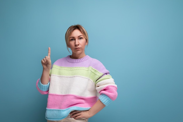 Jolie femme blonde au look décontracté pointant du doigt le mur de l'espace de copie sur fond bleu