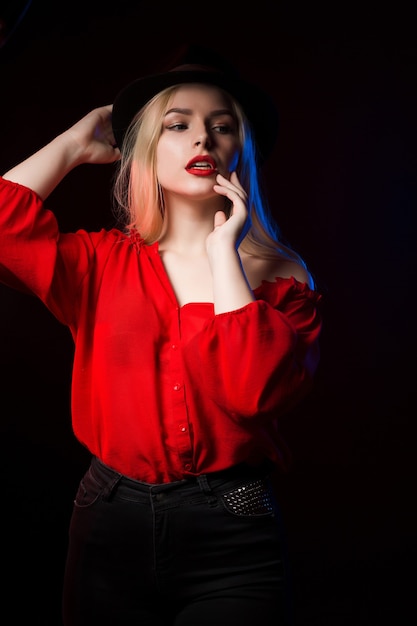 Jolie femme blonde aux lèvres rouges posant dans l'ombre avec une lumière bleue et rouge