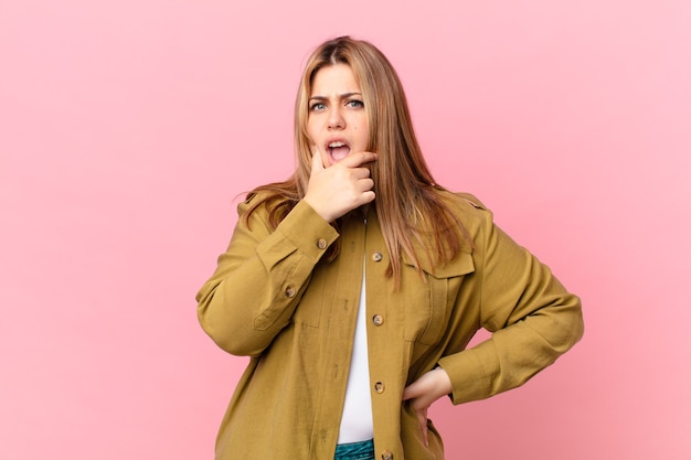 Jolie femme blonde bien roulée avec la bouche et les yeux grands ouverts et la main sur le menton