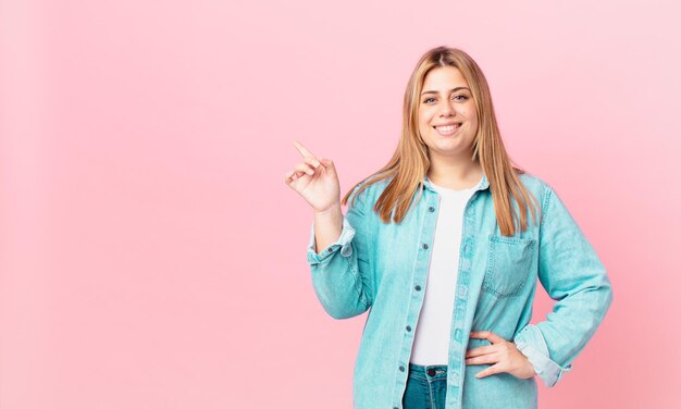 Jolie femme blonde bien roulée souriant joyeusement avec une main sur la hanche et confiante