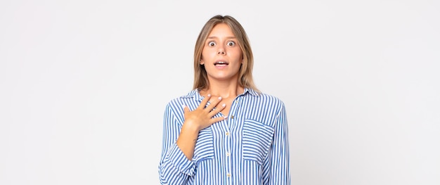 Jolie femme blonde bouche bée sous le choc et l'incrédulité, la main sur la joue et le bras croisés, se sentant stupéfaite et étonnée