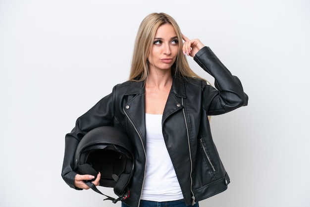 Jolie femme blonde avec un casque de moto isolé sur fond blanc ayant des doutes et pensant