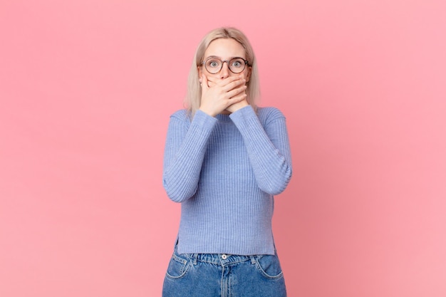 Jolie femme blonde couvrant la bouche avec les mains avec un choqué