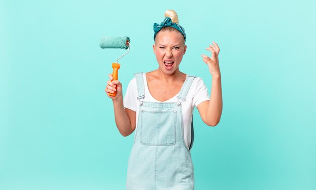 Jolie femme blonde criant avec les mains en l'air et peignant un mur