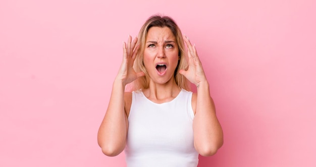 Jolie femme blonde criant avec les mains en l'air se sentant furieuse frustrée stressée et bouleversée