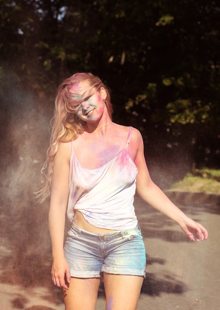 Jolie femme blonde avec du vent dans les cheveux s'amusant avec de la peinture Holi sèche qui explose