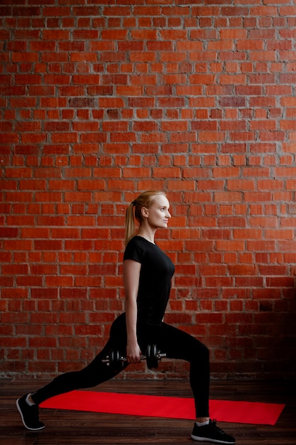 Jolie femme blonde faisant de remise en forme sur l'arrière-plan d'un mur de briques de la maison pendant la quarantaine.