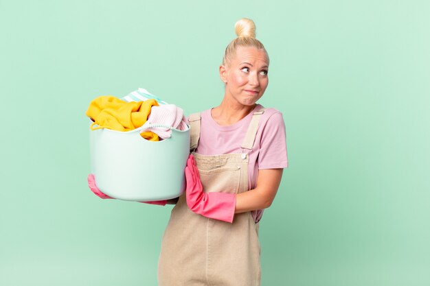 Jolie femme blonde haussant les épaules, se sentant confuse et incertaine, concept de lavage de vêtements