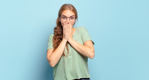 Jolie femme blonde heureuse et excitée, surprise et étonnée couvrant la bouche avec les mains, riant avec une expression mignonne